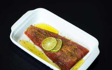 Fresh raw salmon fish steak with spices on ice over dark stone background