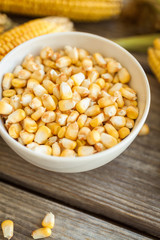 Raw corn on the cob and grains of corn in white bowl on wooden table