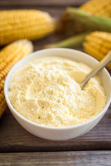 Bowl with corn flour on wooden background