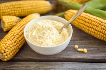 Bowl with corn flour on wooden background