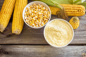 Bowl with corn flour and corn cobs on wooden background