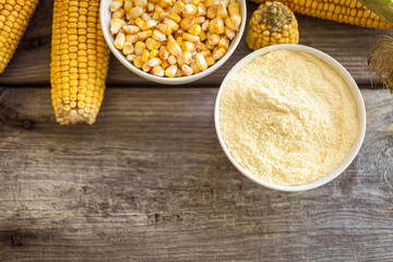 Bowl with corn flour and corn cobs on wooden background