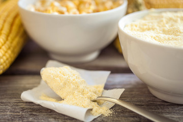 Bowl with corn flour and corn cobs on wooden background