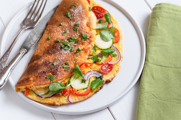 Omelette with zucchini, lamb's lettuce, tomatoes and red pepper on plate. Frittata - italian omelet.