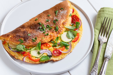 Omelette with zucchini, lamb's lettuce, tomatoes and red pepper on plate. Frittata - italian omelet.