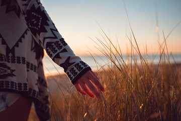 Young woman wearing a jersey with her hand exploring the sand dune grass on the beach with the...