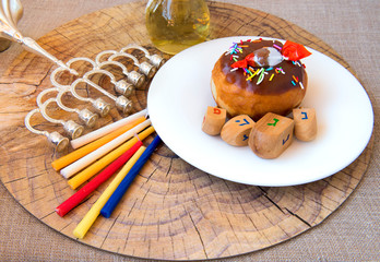Festive donut, menorah, candles, jar of olive oil, dreidels - traditional symbols of Hanukkah Holiday. Hebrew letters on four sides of dreidel in English mean - Great Miracle Happened Here