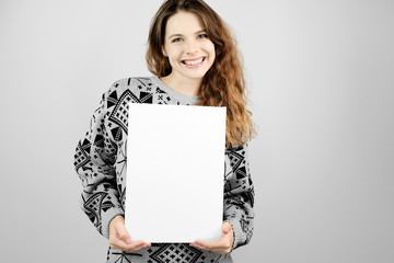 Attractive girl smiling and holding a mockup poster in her hands standing over grey background....