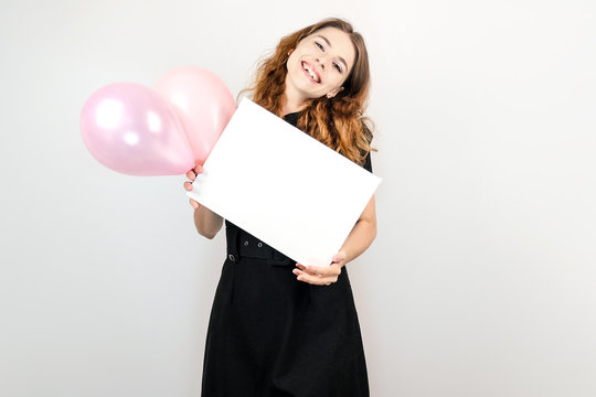 Happy young woman with air balloons in her hands showing a blank canvas board. Mockup poster for message or photo. Copy space.