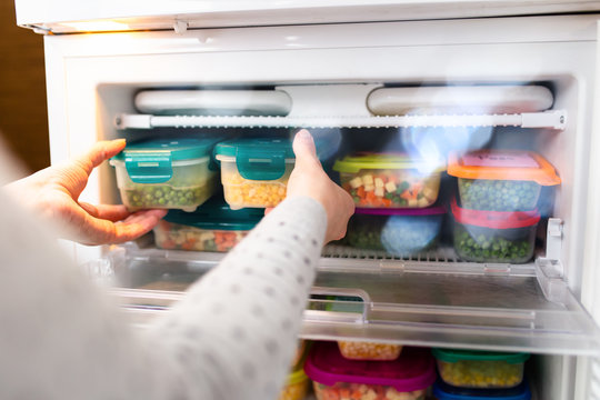 Woman taking containers with frozen peas and corn out from freezer.
