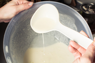 Girls hand is picking up mixture from large cup for baking pancakes.
