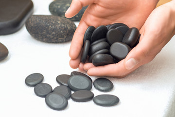 Hot smooth polished massage black stones in man's hands on table of spa salon close up.