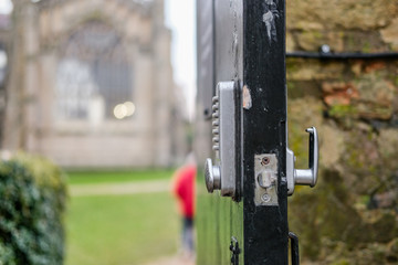 Shallow focus of a combination key pad on an open door leading to a famous, English cathedral. A man can be seen walking along a patch to the building.
