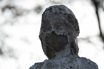 Monument and candles in the cemetery. All Saints Day in Poland. Stone statue in the cemetery. Stone statue in the cemetery. Close-up. Disfigured face statue.