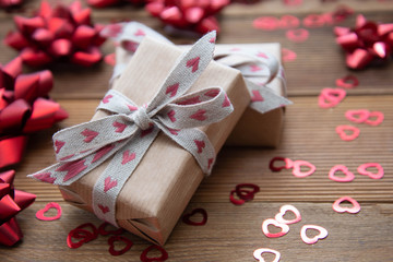 Kraft brown paper gift box with red bows and confetti, on wooden background. Valentine's Day,...