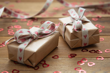 Kraft brown paper gift box with red bows and confetti, on wooden background. Valentine's Day,...