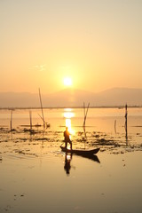 Traditional Fisherman with Canoe Boat at the Lake catching Fish at Sunset Sunrise Sky Background