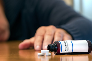 Prescription bottle with Oxycodone tablets on a table over a man wih blur hand.