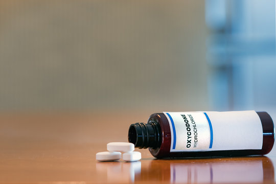 Prescription bottle with Oxycodone tablets on a table.