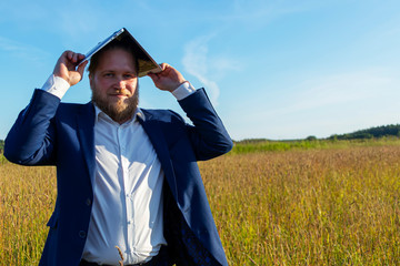 A white caucasian man with a beard holds a laptop on his head outdoors. Concept businessman outdoors.