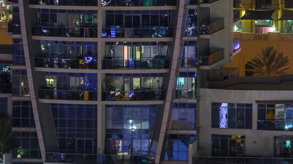 Rows of glowing windows with people in apartment building at night.