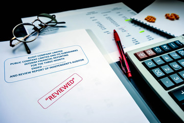 The reviewed financial statement with eyeglass, red pencil, calculator and the edited paper sheet....