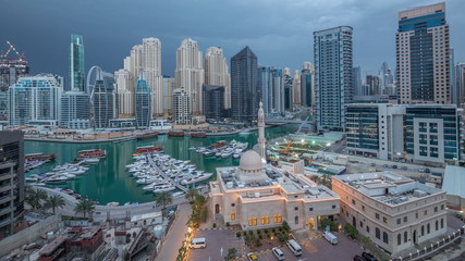Fototapeta na wymiar Yachts in Dubai Marina flanked by the Al Rahim Mosque and residential towers and skyscrapers aerial night to day timelapse.