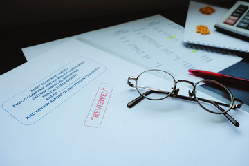 Eye glasses placed on reviewed financial statement with a red pen, calculator and the edited paper. It's important work of the account, finance, internal and external audit must to accurate and timely