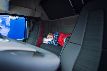 Truck driver sleeping on bed inside truck cabin interior. Trucker lifestyle and people sleeping at job.