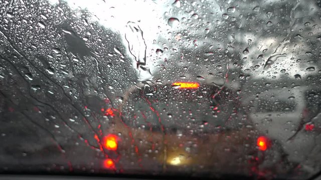 Rain falling on car windshield view. Drive car on traffic jam street at heavy rain storm, inside a car driving,blurred traffic light background.