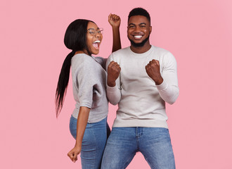 Successful couple celebrating win, dancing over pink background
