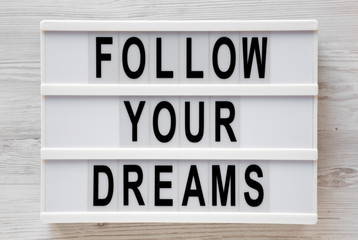 'Follow your dreams' words on a modern board on a white wooden background, top view. Overhead, from above, flat lay. Closeup.