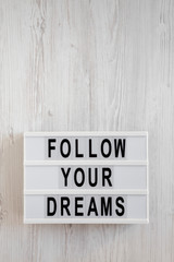 'Follow your dreams' words on a lightbox on a white wooden background, top view. Overhead, from above, flat lay. Copy space.