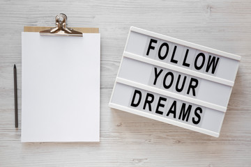 'Follow your dreams' words on a lightbox, clipboard with blank sheet of paper on a white wooden...