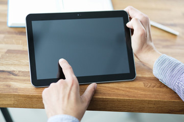 Man's hands holding blank tablet device over a wooden workspace table.