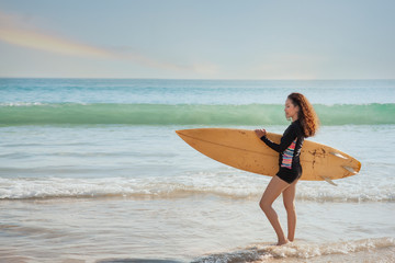 Naklejka na ściany i meble View of beautiful sexy young woman surfer girl with yellow surfboard on a beach at sunset or sunrise.Young asian surfer woman. Good holiday vacation summer concept.