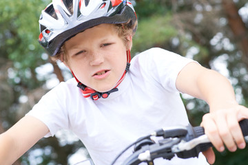 Low angle view of a smiling young boy in safety helmet riding bicycle at the park in summer.