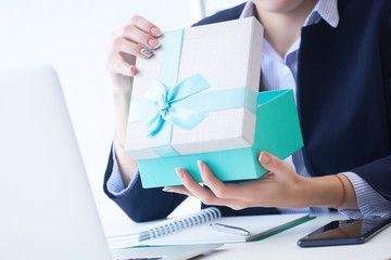 Christmas, any holiday. Office employee received a gift from her colleagues. Closeup woman hands holds gift box on office background.