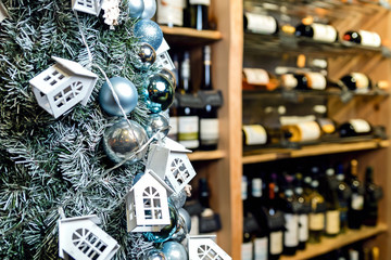 Christmas tree close-up decorated with Christmas balls and toy houses. On the background of shelves with bottles of wine. Blurred background