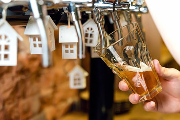 Man's hand pouring pint of beer behind the bar from the tap. Brick wall in the background. Toy houses of white color on the beer taps
