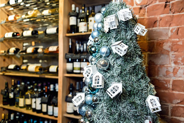 Christmas tree close-up decorated with Christmas balls and toy houses. On the background of shelves with bottles of wine. Blurred background