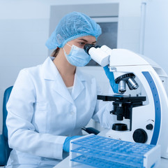 Laboratory worker using modern microscope in mask and gloves