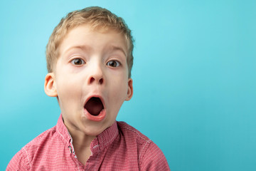 child in a red shirt on a blue background. the child made a surprised face. the boy opened his mouth in shock