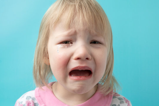little girl in a pink dress on a blue background. the child cries with tears in his eyes