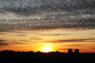 Sunset over the city. Shining sun and orange sky with dark clouds above residential buildings, scenic view