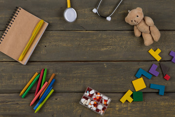 Children's doctor or pediatrician concept - blank notepad, pills, yellow stethoscope, colorful wooden jigsaw puzzles, Teddy bear toy, crayons