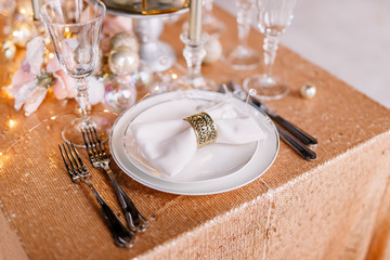 New Year 2020. New Year mood. Table with a gold tablecloth, decorated with candles and tableware for celebration. Festive still life by candlelight. Close-up.