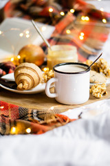 Simple country home breakfast in bed, coffee with milk and homemade pastry on plaid blanket