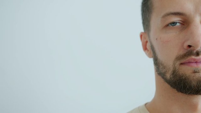 Slow motion of bearded middle-aged man half face on grey-blue background looking at camera with serious facial expression. People and emotions concept.