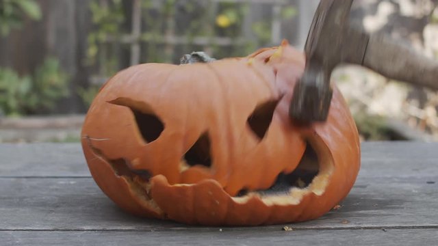 Slow motion close-up of a rotten jack-o-lantern being smashed with a hammer.
